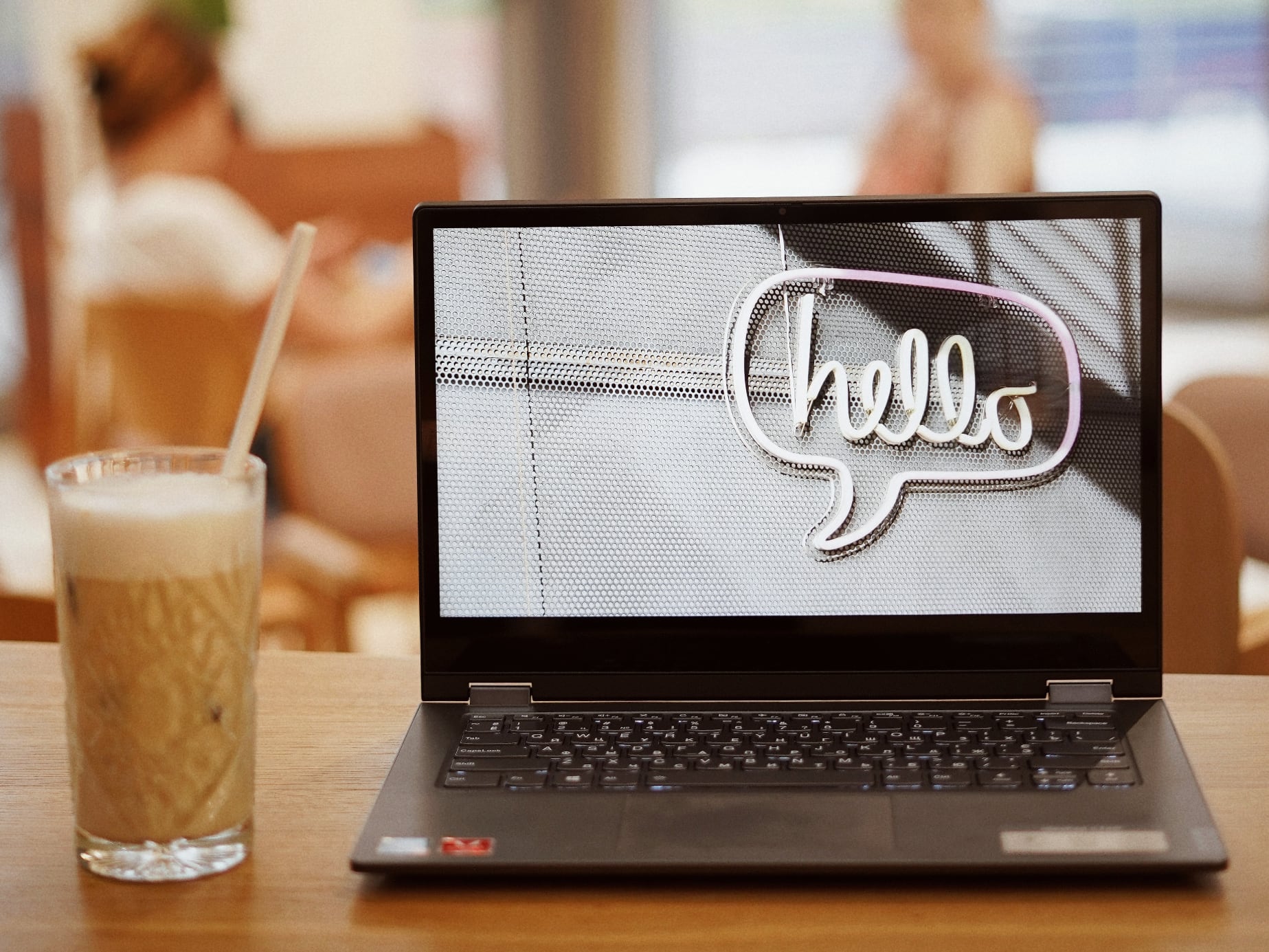 Laptop on desk with glass of cold coffee. Wallpaper of an LED sign saying Hello