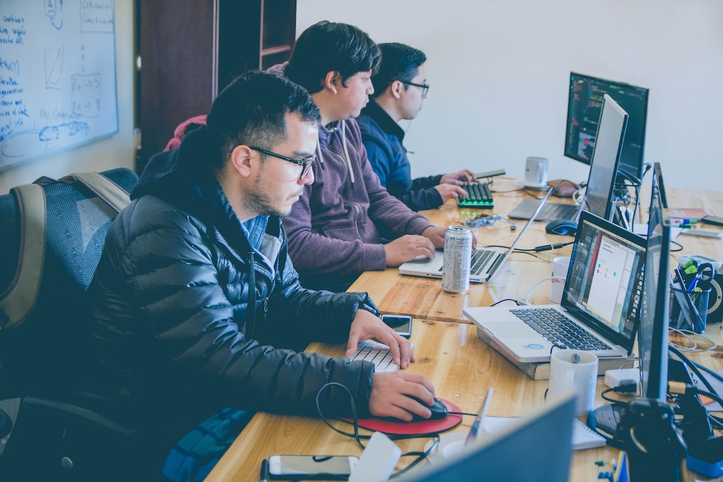 Three people using laptops connected to monitors